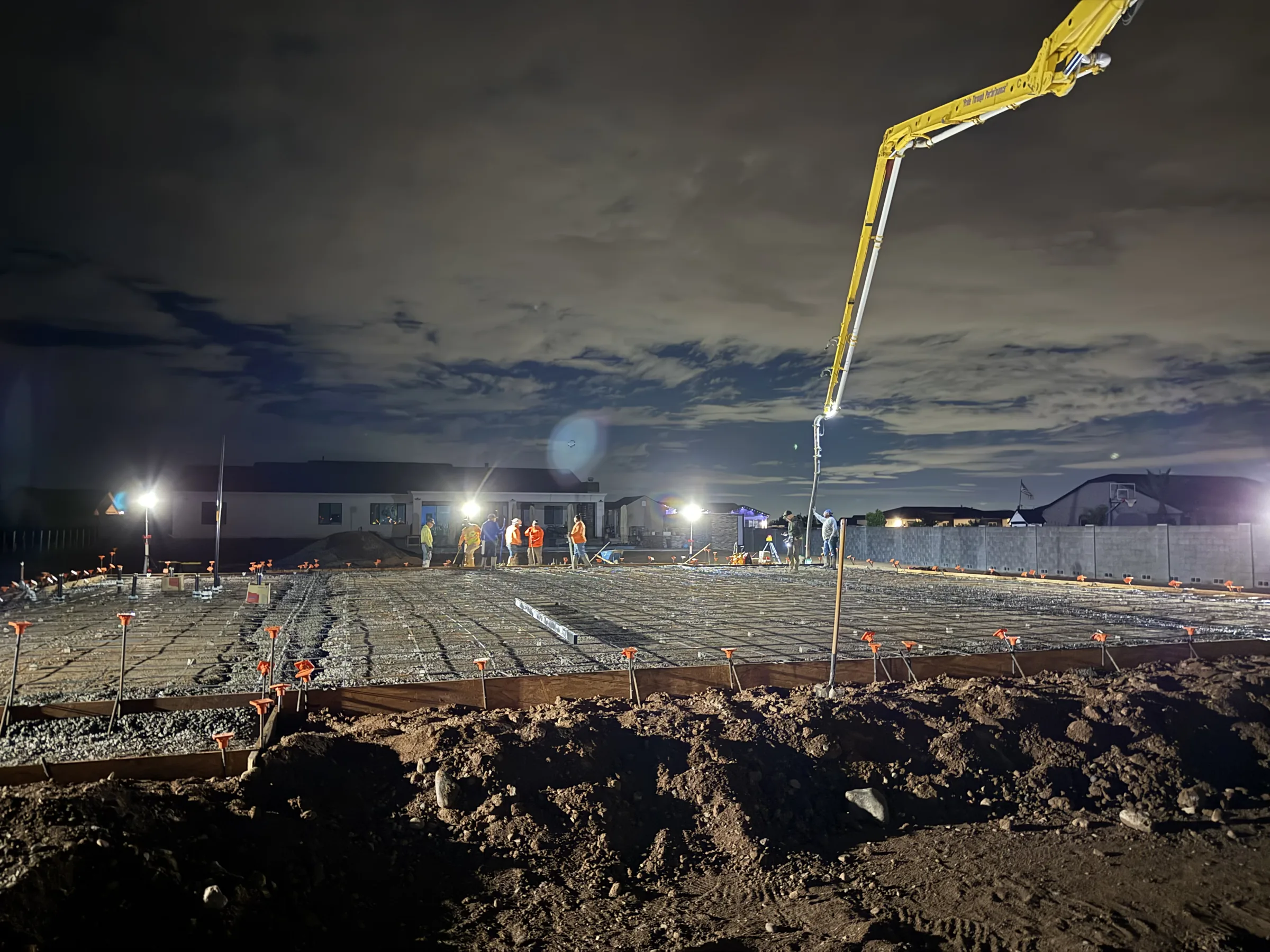 Night concrete pour with a pump boom overhead and the crew placing the slab under work lights