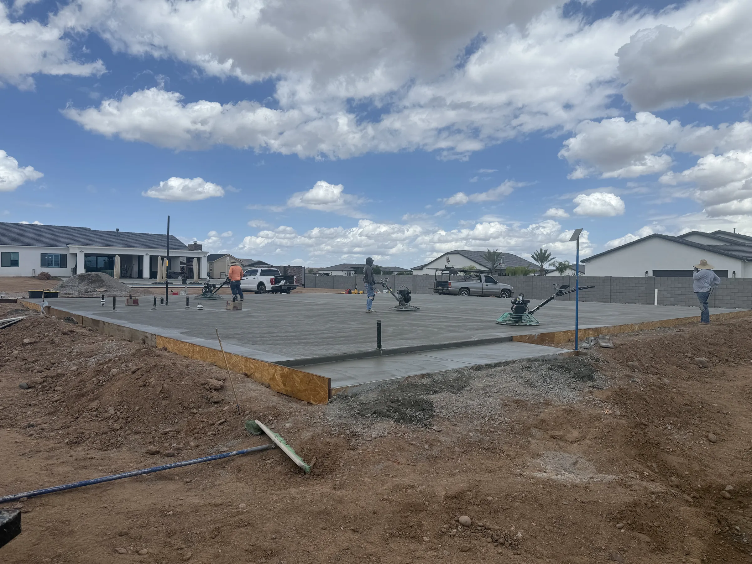 Crew on power trowels finishing a fresh slab, blue sky and block wall behind